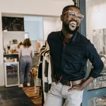 Smiling owner with hands in pockets standing at doorway of clothing store